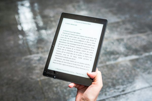 A person holds an e-reader displaying text against a wet pavement background.