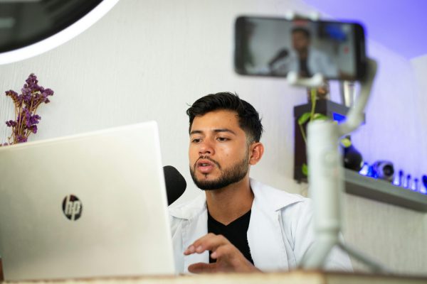 A young man works on a laptop while streaming content online with a smartphone.