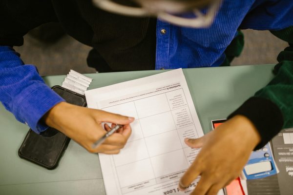 Overhead view of a student writing on a test paper in a classroom setting with a smartphone nearby.